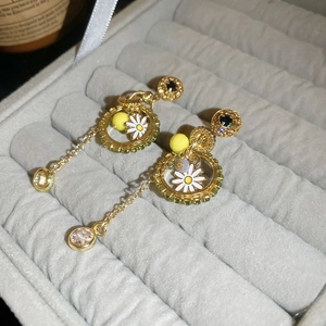 Detail view of asymmetric gold fan earrings with enamel daisies and green crystals