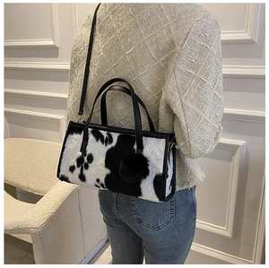 Detail of cow print faux fur handbag with black pom-pom charm worn as a crossbody bag