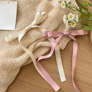 Close-up of pink and cream satin bow hair clips with long ribbons on a wood surface