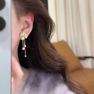 Close-up of pearl tassel earrings on model with elegant floral stud and gold chains