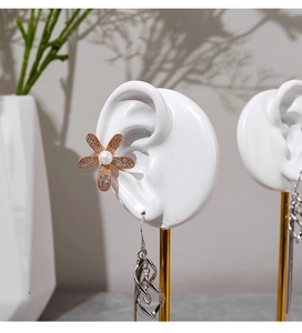 Detail of floral pearl ear clip and silver tassel earring on a white display stand