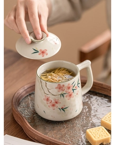 Detail of hand-painted peach blossom ceramic cup with lid and infuser on wooden tray