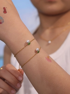 Delicate gold chain bracelet featuring white pearls and green leaf charms on a model wrist