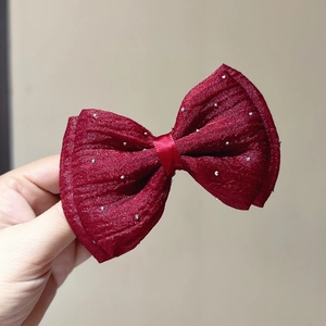 Detail of red mesh bow hair clip with silver glitter accents on a satin fabric base