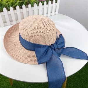 Detail of light beige straw sun hat with a large navy blue ribbon bow on the side