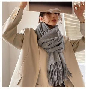 Detailed view of soft grey cashmere-feel scarf with elegant tassels on a female model