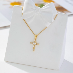 Macro detail of gold cross pendant necklace with heart-shaped zircon on white display stand