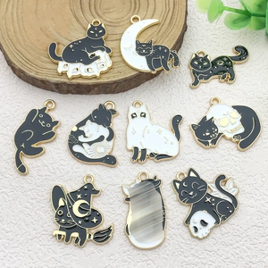 Detailed flat lay of ten black enamel cat charms with gold frames on a beige textured surface