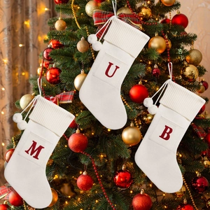 Close-up of white knitted Christmas stockings with red letters M U B on a tree