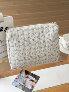 Detailed macro view of cream floral quilted makeup bag with ribbon bow on wooden tray