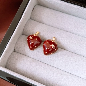 Detailed close-up of dark red enamel strawberry stud earrings with gold accents and zircon