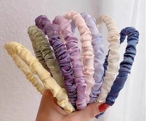 Detail of pleated satin headbands in various soft colors held in a fan shape