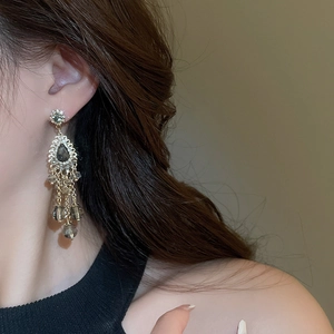Close-up of elegant gold drop tassel earrings with gray gemstones on a female model