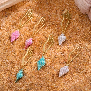 Detalle de los pendientes colgantes de concha en rosa, blanco y azul sobre fondo arena