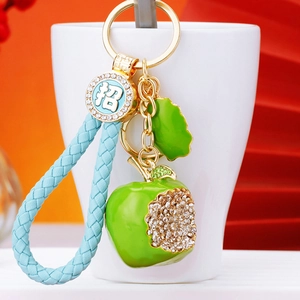 Detail of crystal-encrusted green apple keychain with blue braided strap and gold clasp
