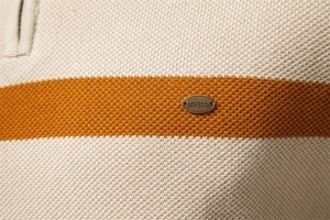Makroaufnahme von cremefarbenem Strickstoff mit orangefarbenen Streifen und Metalldetail