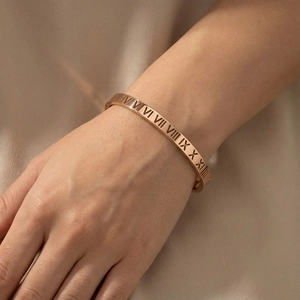 Close-up of rose gold stainless steel bracelet with cutout Roman numeral pattern on wrist