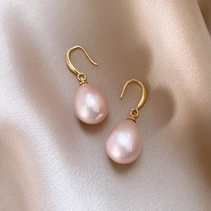 Close-up of pink teardrop pearl earrings with gold hooks on elegant silk fabric
