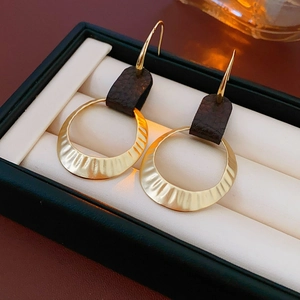 Macro detail of gold hammered metal hoops and dark leather texture on hook earrings