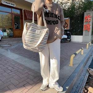 Striped canvas tote bag with woven shoulder strap and knot handles shown on a model