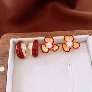 Macro detail of 18k gold-plated pearl flower earrings and red enamel hoops on velvet