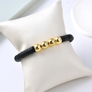 Close-up of black disc beads and gold spherical beads bracelet on white display pillow