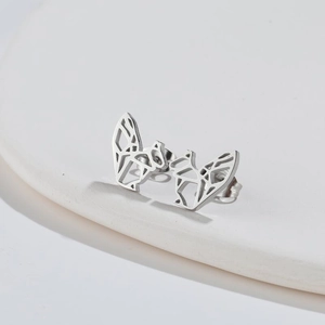 Detailed macro view of silver stainless steel origami fox stud earrings on a ceramic base