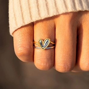 Dual-tone silver and gold heart layered ring worn on hand with cozy knitwear background