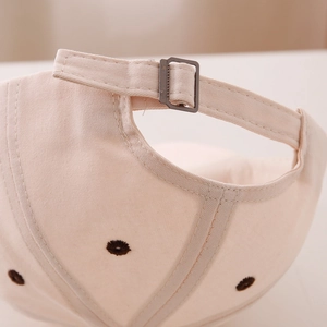 Detail view of adjustable metal buckle and stitching on beige cotton baseball cap