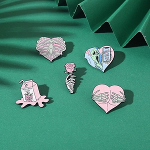 Detailed macro view of pink enamel pins featuring skeleton hearts and scream ghost on green fabric