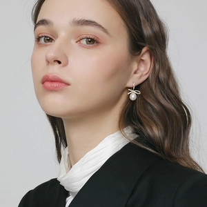 Elegant gold bow earrings with shimmering crystals and white pearls shown on a model