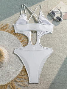 Detailed flat lay of white cutout swimsuit with metal rings and vacation accessories