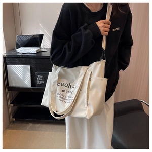 Detailed view of white canvas tote bag with graphic text and shoulder strap worn by model