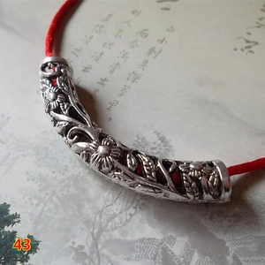 Macro detail of antique silver tube bead with floral hollow carvings and red woven cord
