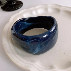 Detailed view of wide resin bangle with dark blue marble texture on white plate