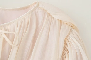 Dettaglio del tessuto plissettato perlato con elegante fiocco su un abito corto beige