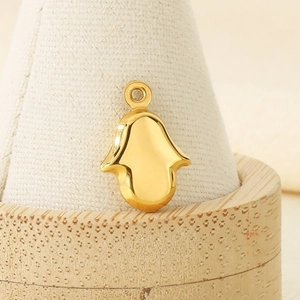 Macro shot of polished gold Hamsa Hand pendant on a beige jewelry display stand