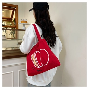 Detailed view of red canvas tote bag with apple print carried by a model in a cafe