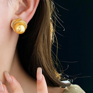 Close-up of a gold pearl earring with cubic zirconia accents worn by a female model