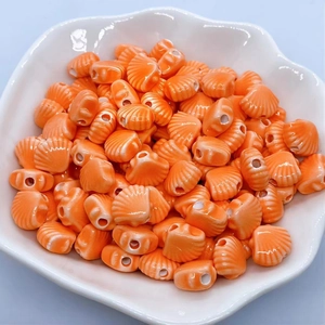 Detailed view of orange and white shell-shaped ceramic beads in a white floral bowl