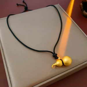 Detailed close-up of a matte gold gourd pendant on a black adjustable woven cord