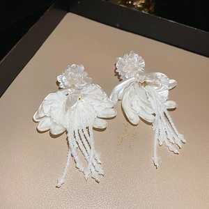 Macro detail of white floral tassel earrings with beaded fringe on a beige leather texture