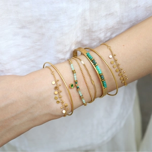 Detail of bohemian gold layered bracelets with green beads and Evil Eye charm pendant