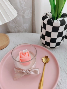 Detail of pink rose-shaped soy candle in glass cup with champagne ribbon and bow