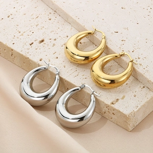 Polished gold and silver teardrop earrings displayed on a beige stone and silk backdrop