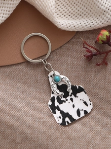 Western style keychain with cow print charm and turquoise horseshoe on rustic background