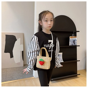 Detail of beige straw crossbody bag with a cute red strawberry doll for kids