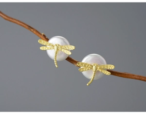 Detailed close-up of golden dragonfly pearl earrings hanging on a thin wooden branch