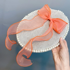 Close-up of a velvet round box featuring a large coral organza bow and pearl trim