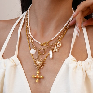 Layered gold necklace featuring freshwater pearls, a sun face mask, and a cross pendant